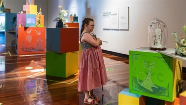 A girl is looking at an art piece with her arms crossed.