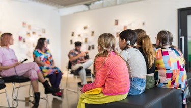 Children and adults are sitting on chairs in a circle discussing the exhibition Fresh Eyes.