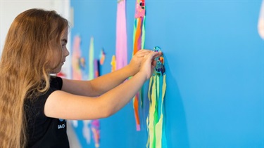 A young girl is gluing her decorative jellyfish to the wall.