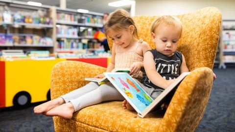 Two children reading books on yellow chair