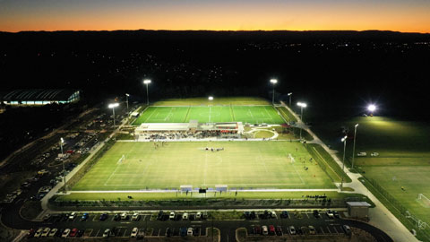 Aerial of two sports fields lit up at sunset.