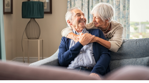 Two people hugging on a couch smiling at one another