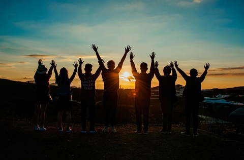 group of youths facing a sunset with arms in the air