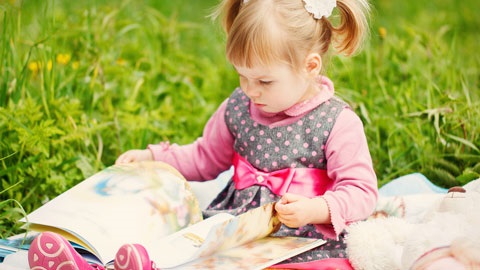 young girl sitting on grass reading book