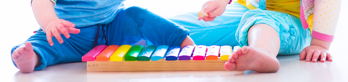 Two babies sitting behind a xylophone