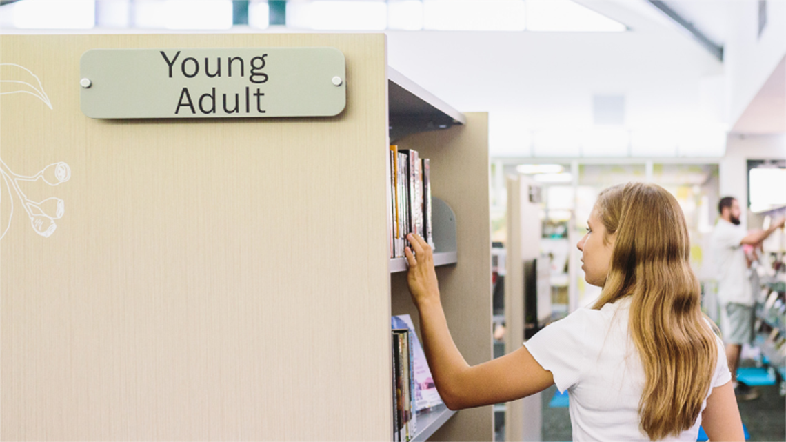 Young girl looking through books in a public library