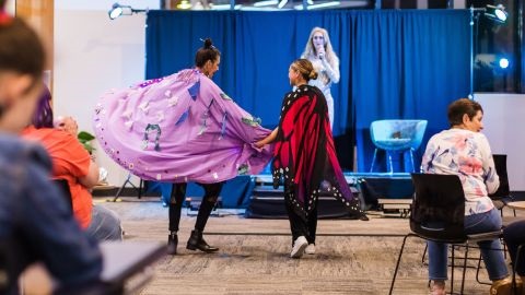 Two people on catwalk wearing coloured capes