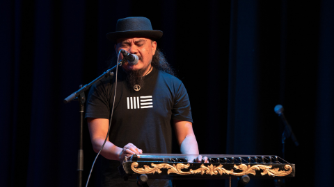 Efiq Zulfiqar is standing behind an instrument and singing into a microphone against a black backdrop.