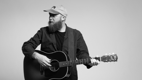 a man with a beard and cap playing guitar looking away from the camera