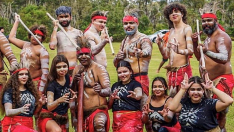 a group of young indigenous young peoples standing in a group with traditional makeup and outfits posing