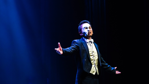 Man with dark background and spotlight on him with arms wide open and singing