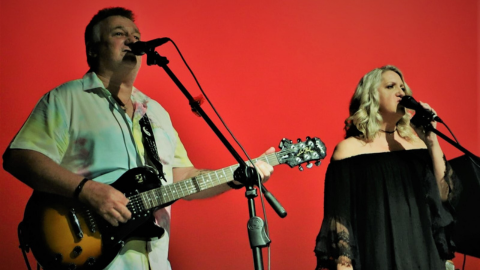 Image of a male musician singing and playing guitar alongside a female singer