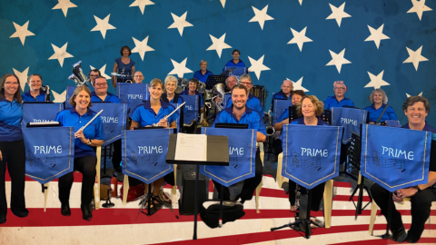 Image of the band sitting with instruments in front of the American flag.