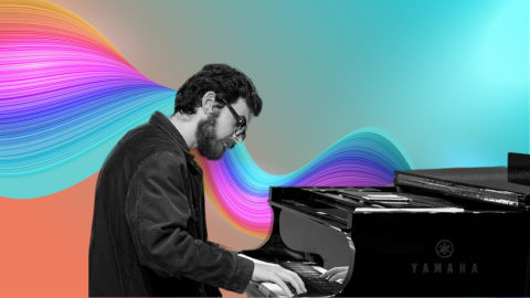 man with glasses head down playing a black piano with rainbow background