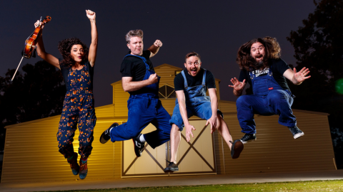 four people jumping in air and smiling at camera at night in front of a barn