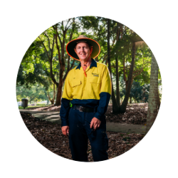 Man wearing a yellow Council uniform and straw hat looking at the camera with trees behind him.