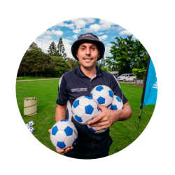 Mitch Jokelainen smiling on a sports field holding 4 soccer balls