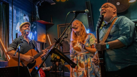 three people singing holding guitars