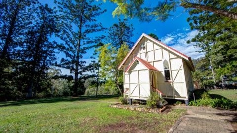 A green lawn with a beautiful old wooden building on it. There are tall trees and blue sky around the wooden building.