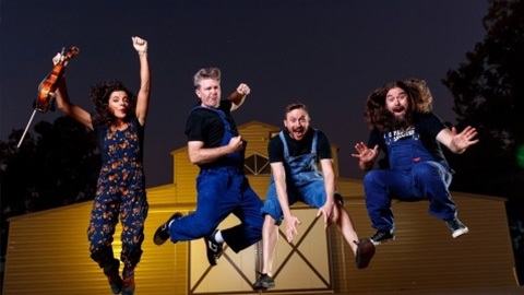 Musicians jumping in front of a barn 