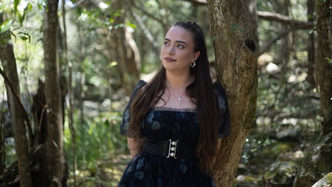 Singer-songwriter Jade Clark, leaning against a tree in the bush.