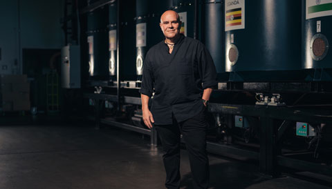 Phillip Di Bella standing in front of large, silver coffee bean roasters