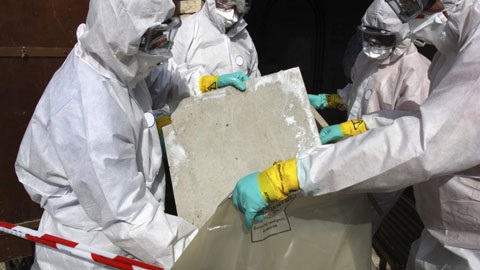 4 people in white protective suits with masks and gloves holding and wrapping asbestos products