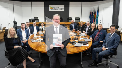 Link to video - image shows Mayor holding budget document with other councillors seated at a table behind him.