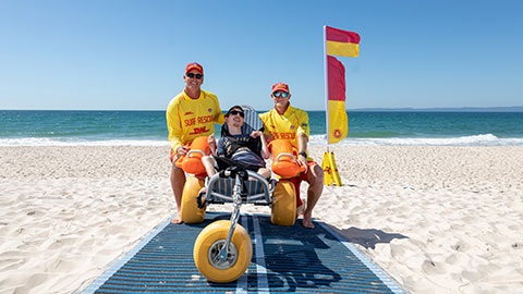 Bribie Island Surf Life Saving Club with community member in beach wheelchair on Woorim Beach beach matting