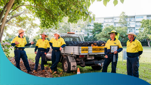 A group of 5 men in hi-vis shirts standing around a ute talking