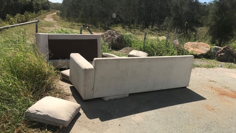 2 couches illegally dumped with cushions lying nearby at an entranceway to bushland.